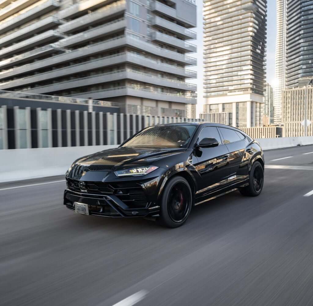FX Productions Canada A black Lamborghini Urus SUV drives on a city street with modern high-rise buildings in the background, showcasing Toronto Video Production excellence. Toronto Video Production Company