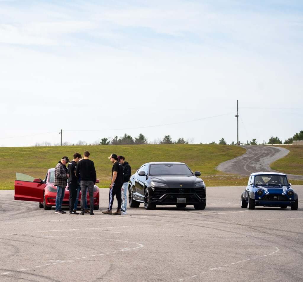 FX Productions Canada A group of people gather near a red car, with a black SUV and a blue compact car parked on an open paved area under a clear sky—an ideal scene for a Toronto Video Production shoot by FX Productions Canada. Toronto Video Production Company
