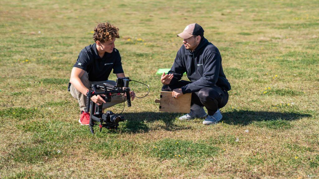 FX Productions Canada Two people crouch on grass, examining a professional camera setup; one holds a clipboard and gestures while the other adjusts the camera equipment for FX Productions Canada, a leading Toronto Video Production company. Toronto Video Production Company