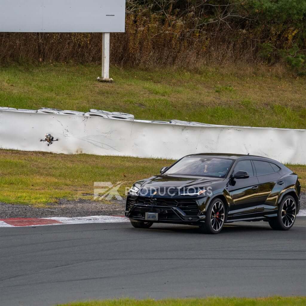 FX Productions Canada A black Lamborghini SUV driving on a racetrack, captured by Toronto Video Production, with a white barrier and grassy area in the background. Toronto Video Production Company