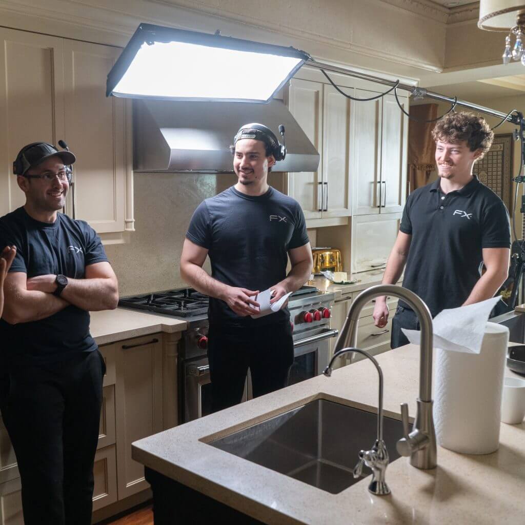 FX Productions Canada Three men in black shirts stand and talk in a kitchen set, surrounded by professional lighting equipment and filming gear from Toronto Video Production experts. Toronto Video Production Company