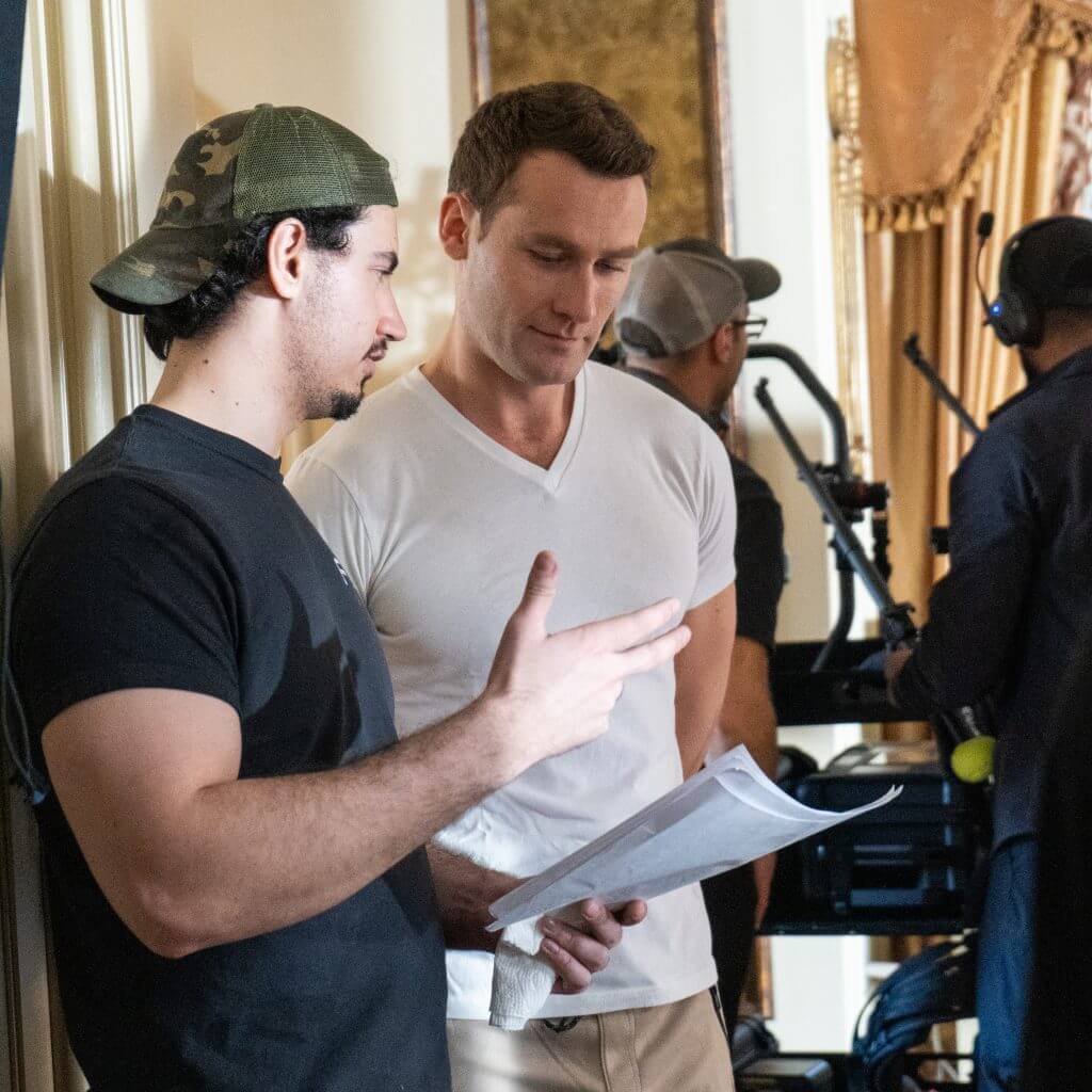 FX Productions Canada Two men stand indoors reviewing a document together, while others with filming equipment from FX Productions Canada work in the background. Toronto Video Production Company