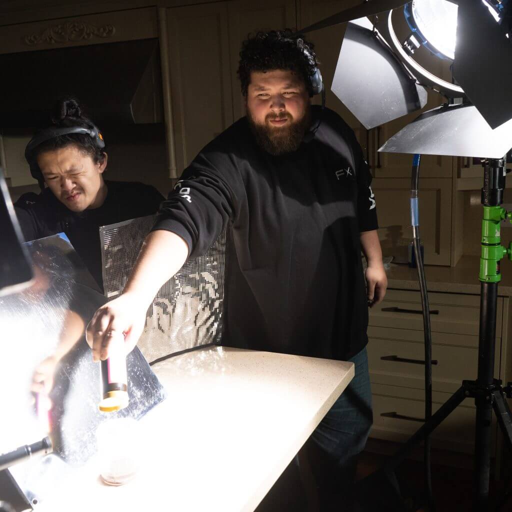 FX Productions Canada Two people from FX Productions Canada work on a food photography setup in a kitchen, adjusting lighting and holding a tool over a plate on the counter. Toronto Video Production Company