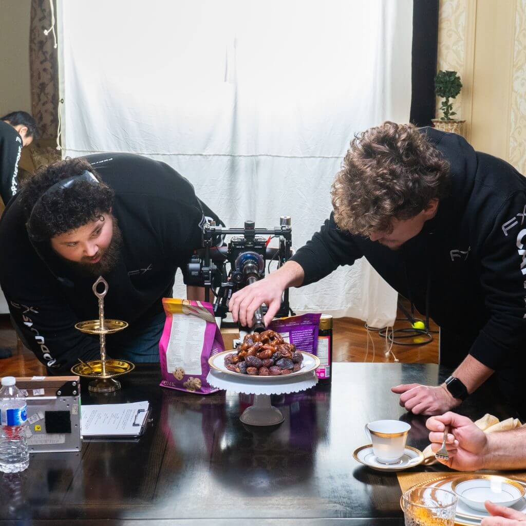 FX Productions Canada Two men from a Toronto Video Production company set up a camera to film or photograph a plate of dates on a cake stand, carefully adjusting the arrangement on a dining table set for tea. Toronto Video Production Company