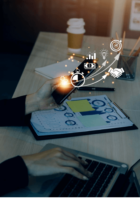 FX Productions Canada A person holds a smartphone with financial and business icons overlaid, while another hand types on a laptop near documents and a coffee cup—capturing the dynamic energy of a Toronto Video Production workspace. Toronto Video Production Company