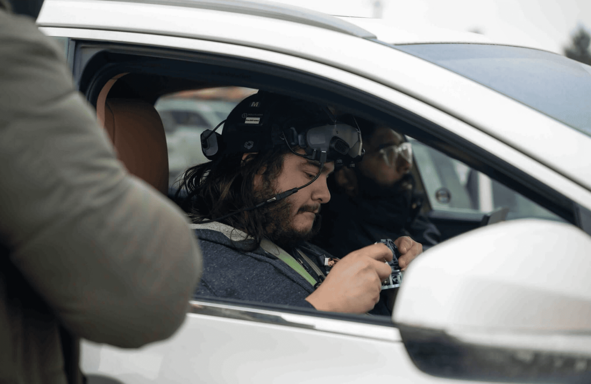 FX Productions Canada Two people sit inside a white car; one wears a headset with a microphone and operates a device, while another sits in the passenger seat during an FX Productions Canada shoot. Toronto Video Production Company