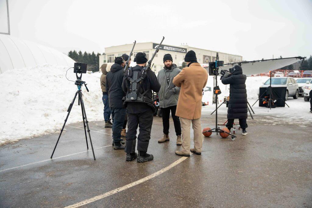 FX Productions Canada A film crew from FX Productions Canada stands outdoors on a snowy day, setting up equipment and having a discussion in a parking lot with snowbanks in the background. Toronto Video Production Company