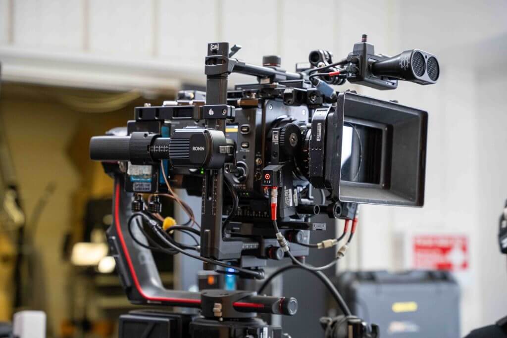 FX Productions Canada Professional video camera mounted on a tripod with various cables and accessories attached, photographed indoors with a blurred background—ideal gear for any Toronto Video Production or FX Productions Canada project. Toronto Video Production Company