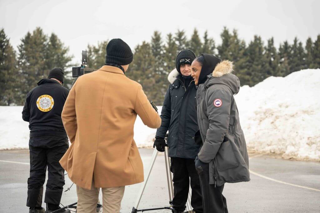 FX Productions Canada Four people stand outdoors in winter clothing near a camera on a tripod, with snowbanks and trees visible in the background—an authentic behind-the-scenes moment from a Toronto Video Production team at work. Toronto Video Production Company