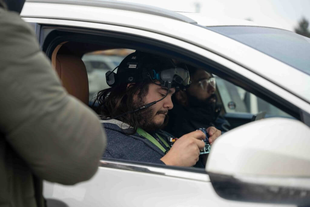 FX Productions Canada A person sits in the driver's seat of a car wearing VR goggles with cables, another in the passenger seat, and a third standing outside—the scene captured by FX Productions Canada, a leading Toronto Video Production company. Toronto Video Production Company