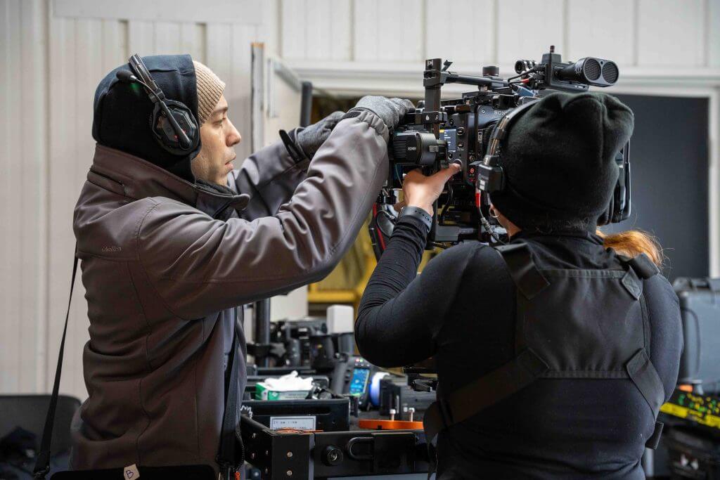 FX Productions Canada Two crew members wearing headsets and winter clothing adjust a professional video camera on set in an indoor setting, showcasing the expertise of FX Productions Canada, a leading Toronto Video Production company. Toronto Video Production Company