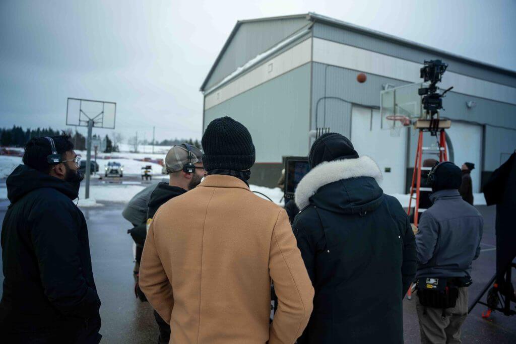 FX Productions Canada A group of people wearing winter clothing stands outside near a basketball hoop, observing a camera setup on a ladder beside a building—capturing behind-the-scenes moments with Toronto Video Production experts. Toronto Video Production Company