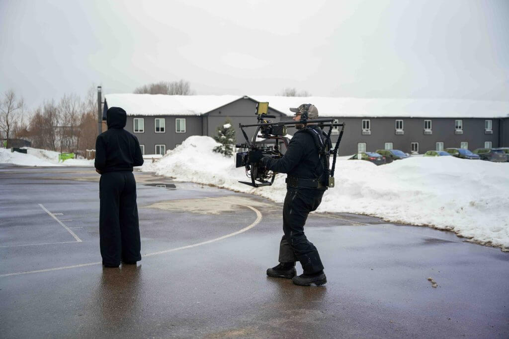FX Productions Canada A person in black stands on a wet outdoor basketball court in winter as a cameraman from FX Productions Canada films with a shoulder-mounted rig; snow piles are in the background. Toronto Video Production Company