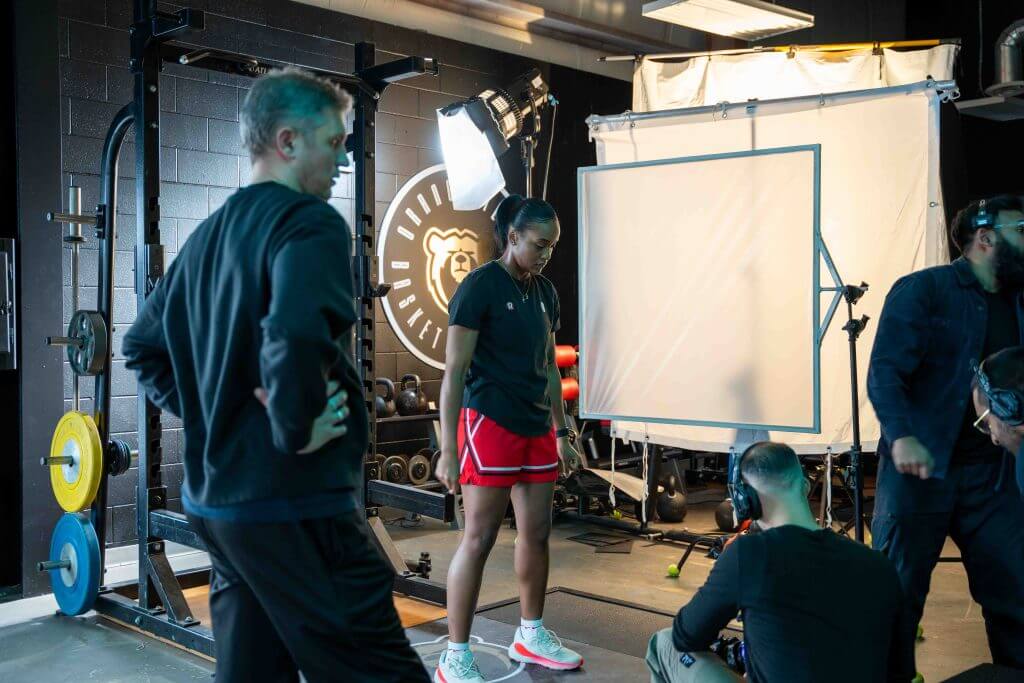 FX Productions Canada A woman in sportswear stands in a gym set as crew members and lighting equipment from a Toronto Video Production company prepare for a video or photo shoot. Toronto Video Production Company