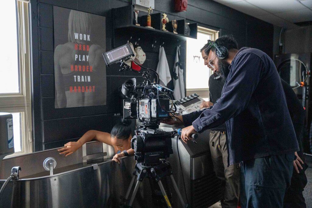 FX Productions Canada A film crew from Toronto Video Production records a person partially submerged in a metal tub, with a camera and clapperboard in a gym-like setting featuring a motivational poster on the wall. Toronto Video Production Company