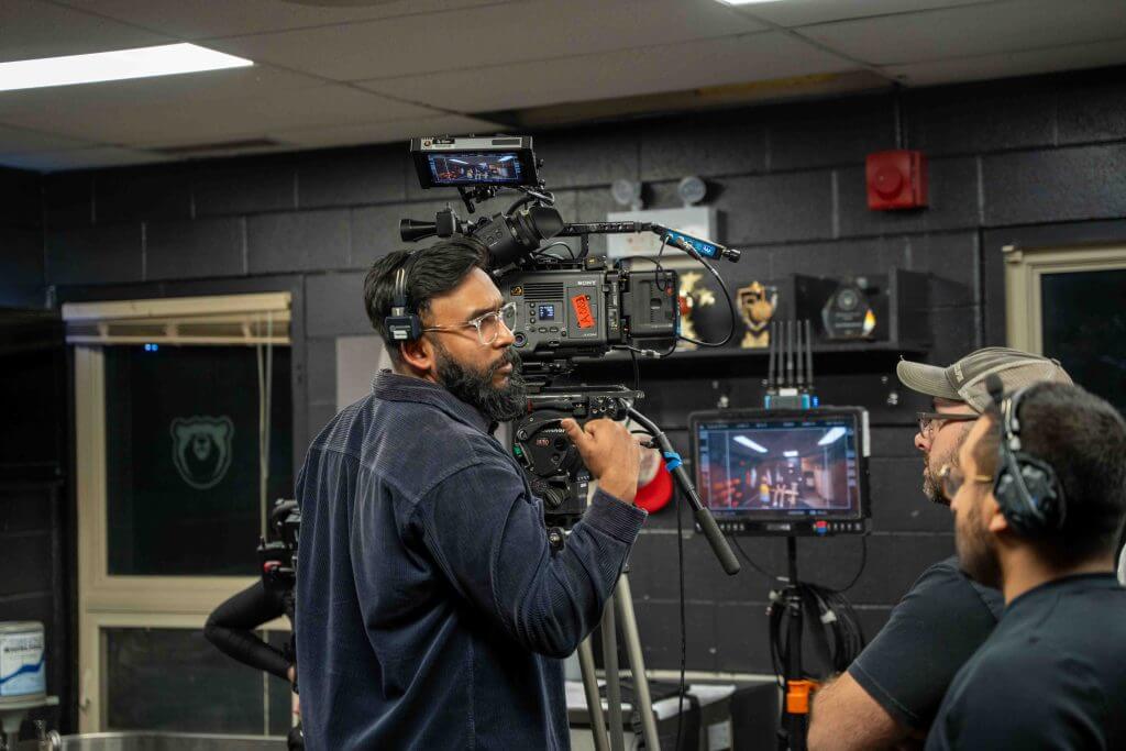 FX Productions Canada A camera operator films a scene indoors while talking to two crew members; monitors and equipment are visible in the background at this Toronto Video Production shoot. Toronto Video Production Company