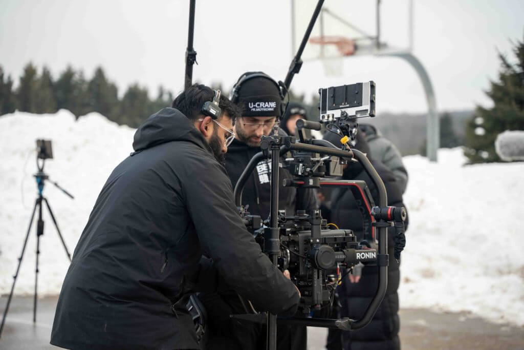 FX Productions Canada Two people from FX Productions Canada adjust a professional video camera setup outdoors in a snowy area, with a basketball hoop and other Toronto Video Production equipment visible in the background. Toronto Video Production Company