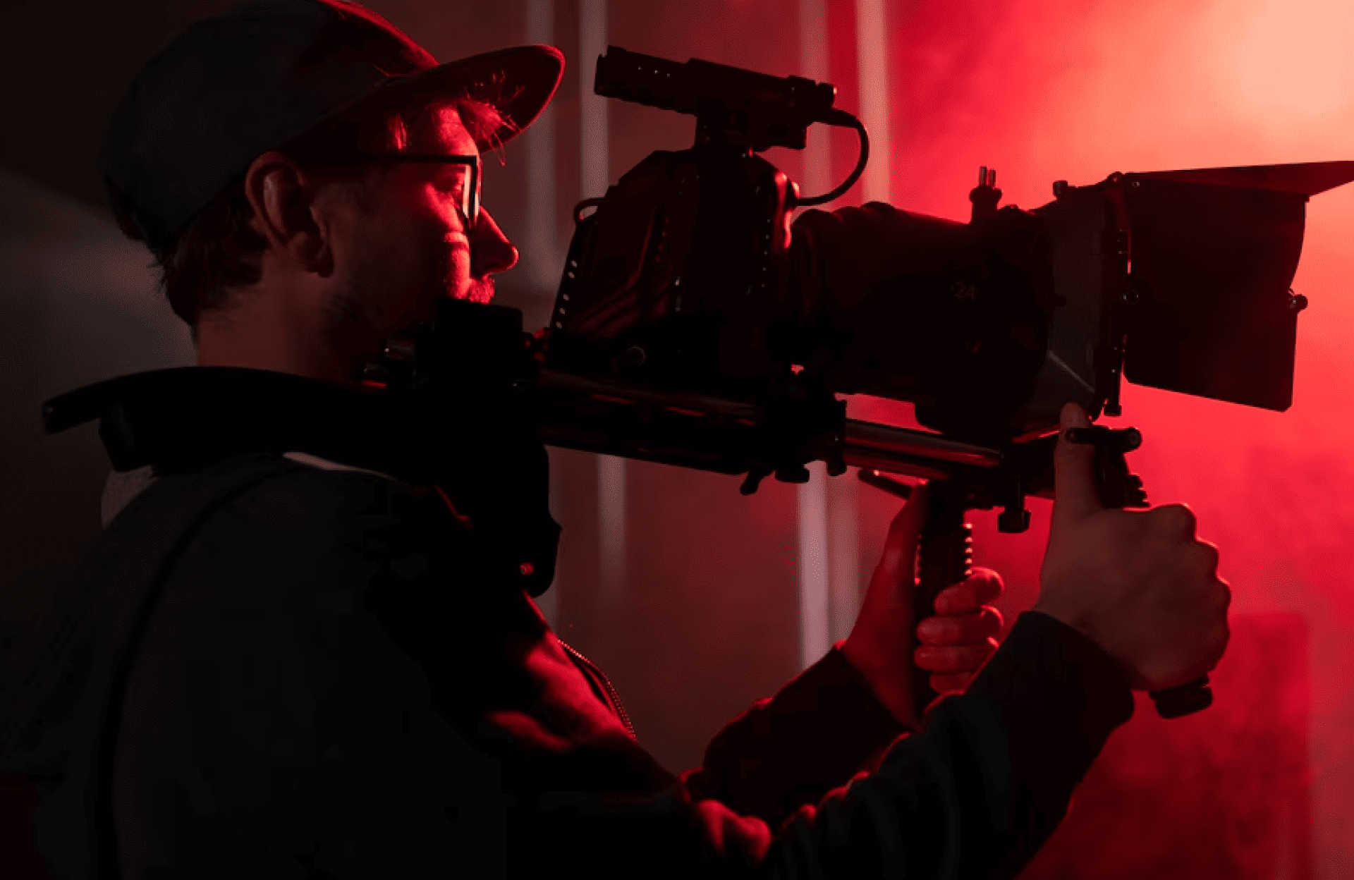 FX Productions Canada A person wearing a cap and glasses operates a professional video camera rig in dramatic red lighting, capturing the dynamic energy of an FX Productions Canada project. Toronto Video Production Company