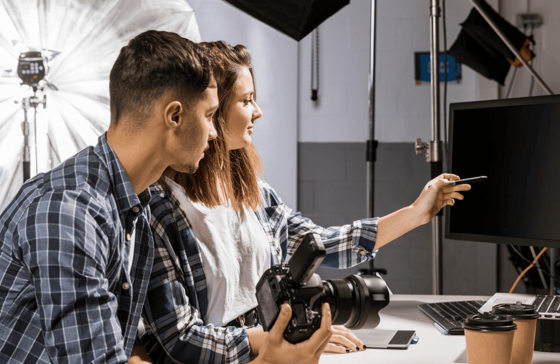 FX Productions Canada Two people in a photography studio sit at a desk with a camera, reviewing images on a computer monitor, surrounded by lighting equipment and props—capturing the creative energy of FX Productions Canada. Toronto Video Production Company
