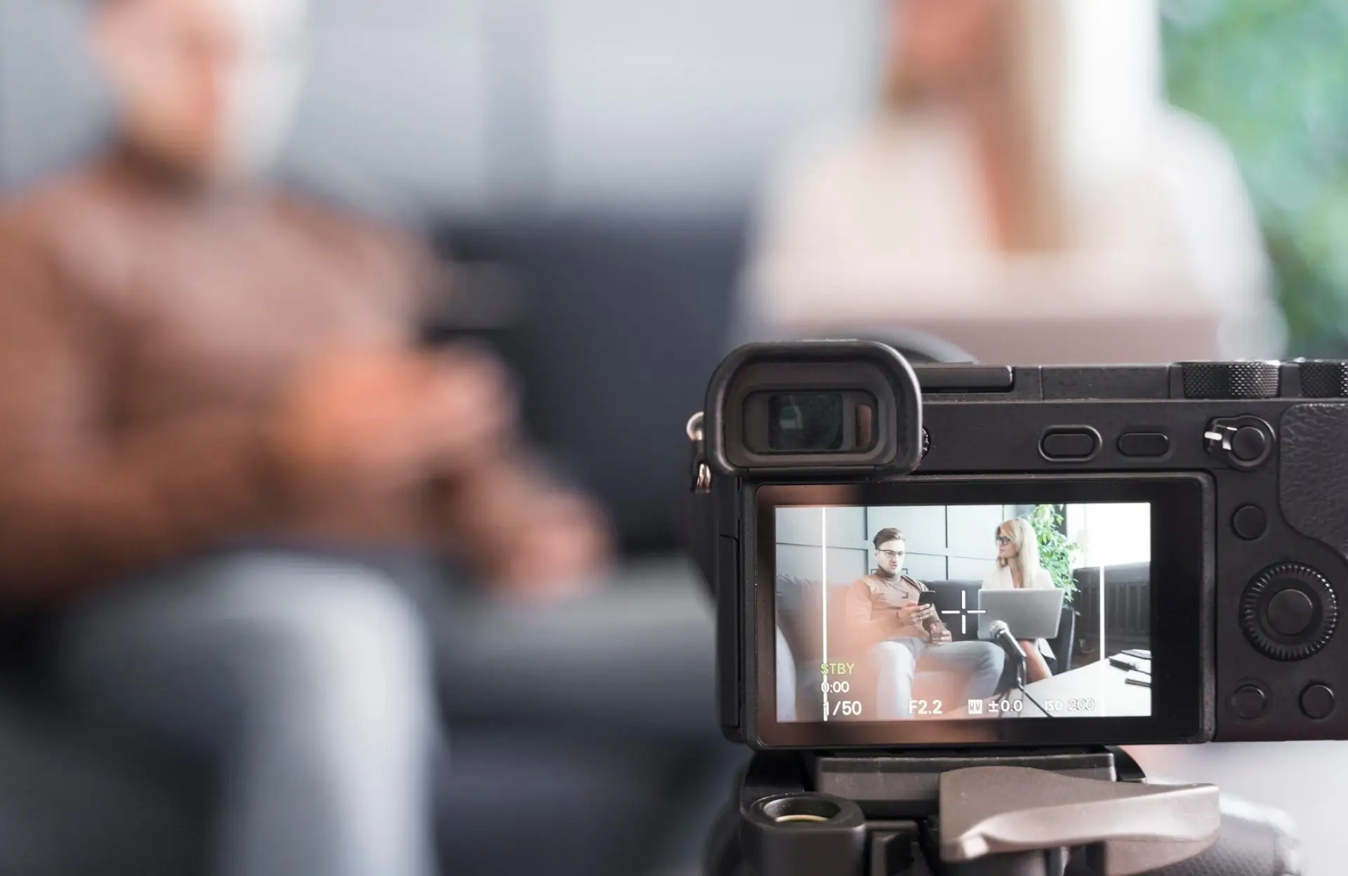 FX Productions Canada A digital camera records two people sitting on a sofa, both out of focus in the background but visible on the camera’s display screen. Toronto Video Production Company
