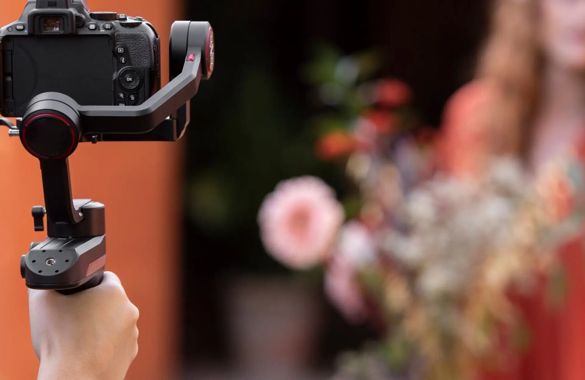 FX Productions Canada A person holds a camera mounted on a handheld stabilizer, aimed at a blurred subject and flowers in the background. Toronto Video Production Company
