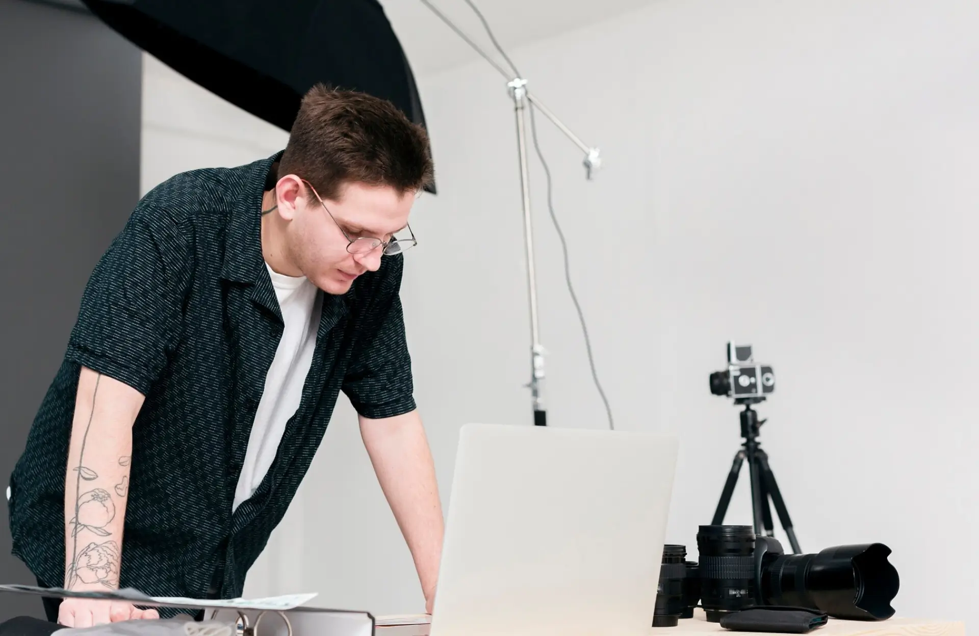 FX Productions Canada A man with glasses stands at a desk, looking at a laptop. Photography equipment, including cameras and lenses, is set up in the background. Toronto Video Production Company