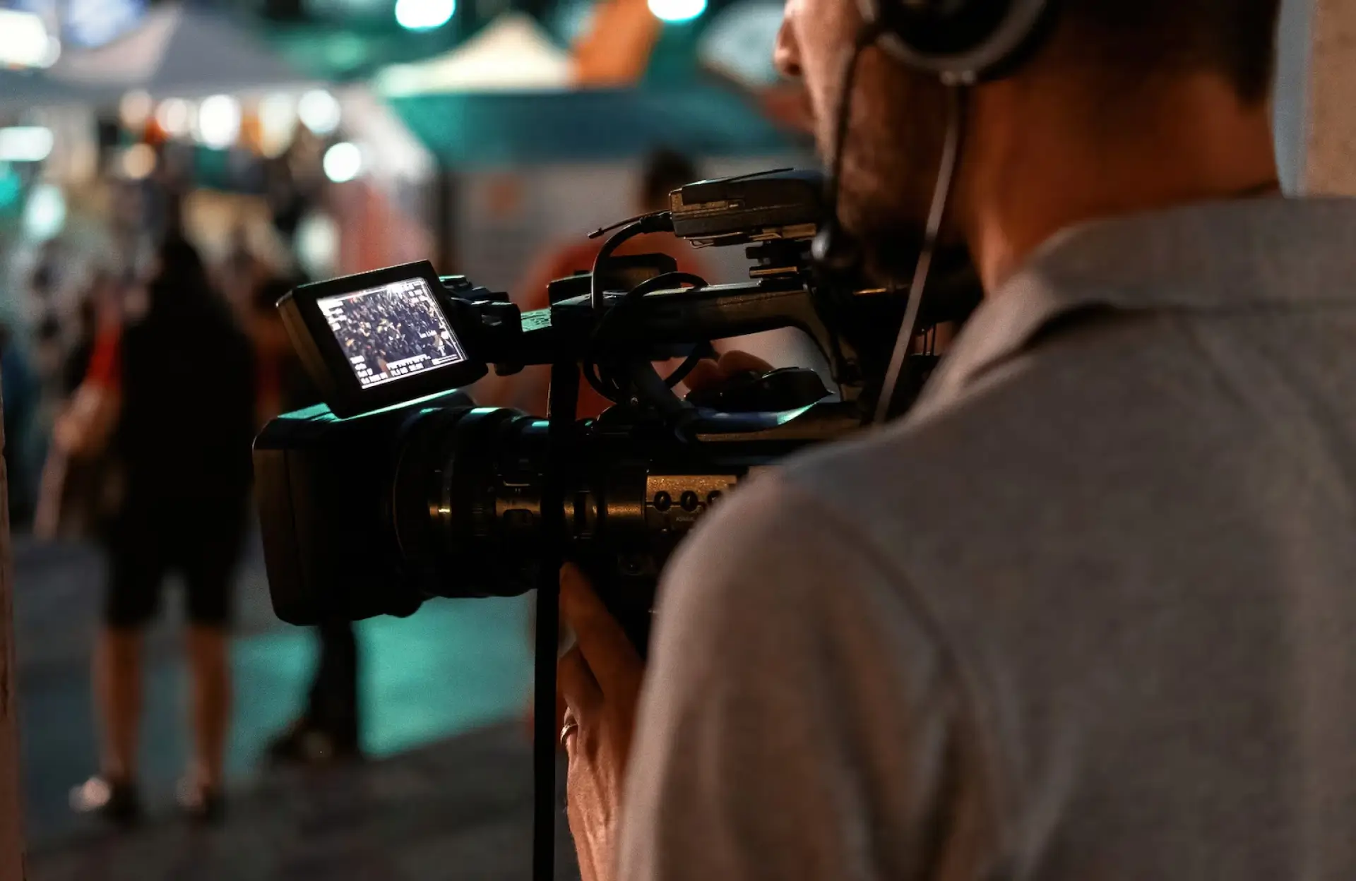 FX Productions Canada A person wearing headphones operates a professional video camera, capturing footage at an outdoor event with blurred people and lights in the background. Toronto Video Production Company