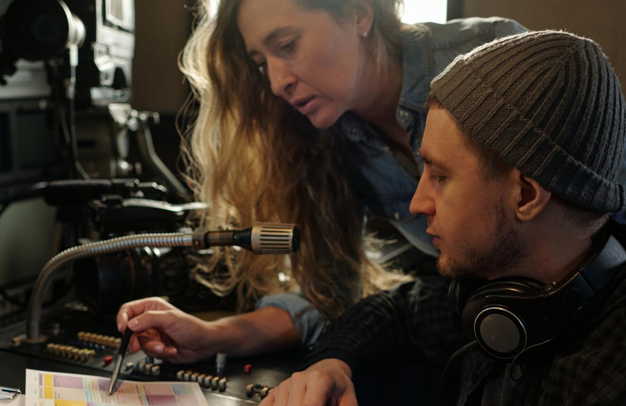FX Productions Canada Two people collaborate at an audio control panel, discussing color-coded notes—a scene showcasing video production services in Toronto and a passion for cinematic storytelling. One wears headphones and a beanie, while the other points with a pen. Toronto Video Production Company