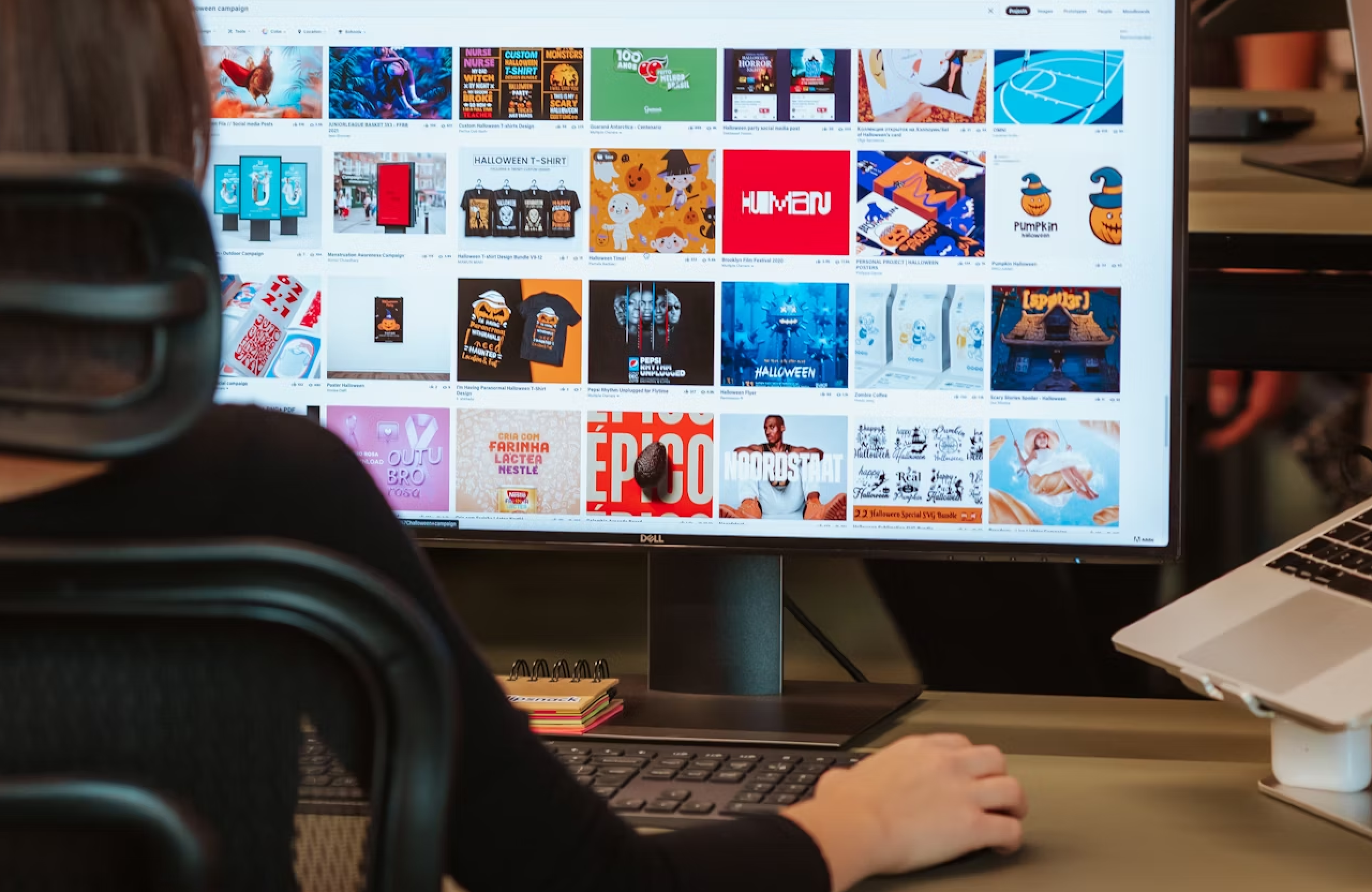 FX Productions Canada Person sitting at a desk using a mouse, viewing a large computer monitor displaying a grid of colorful digital images and graphics. Toronto Video Production Company