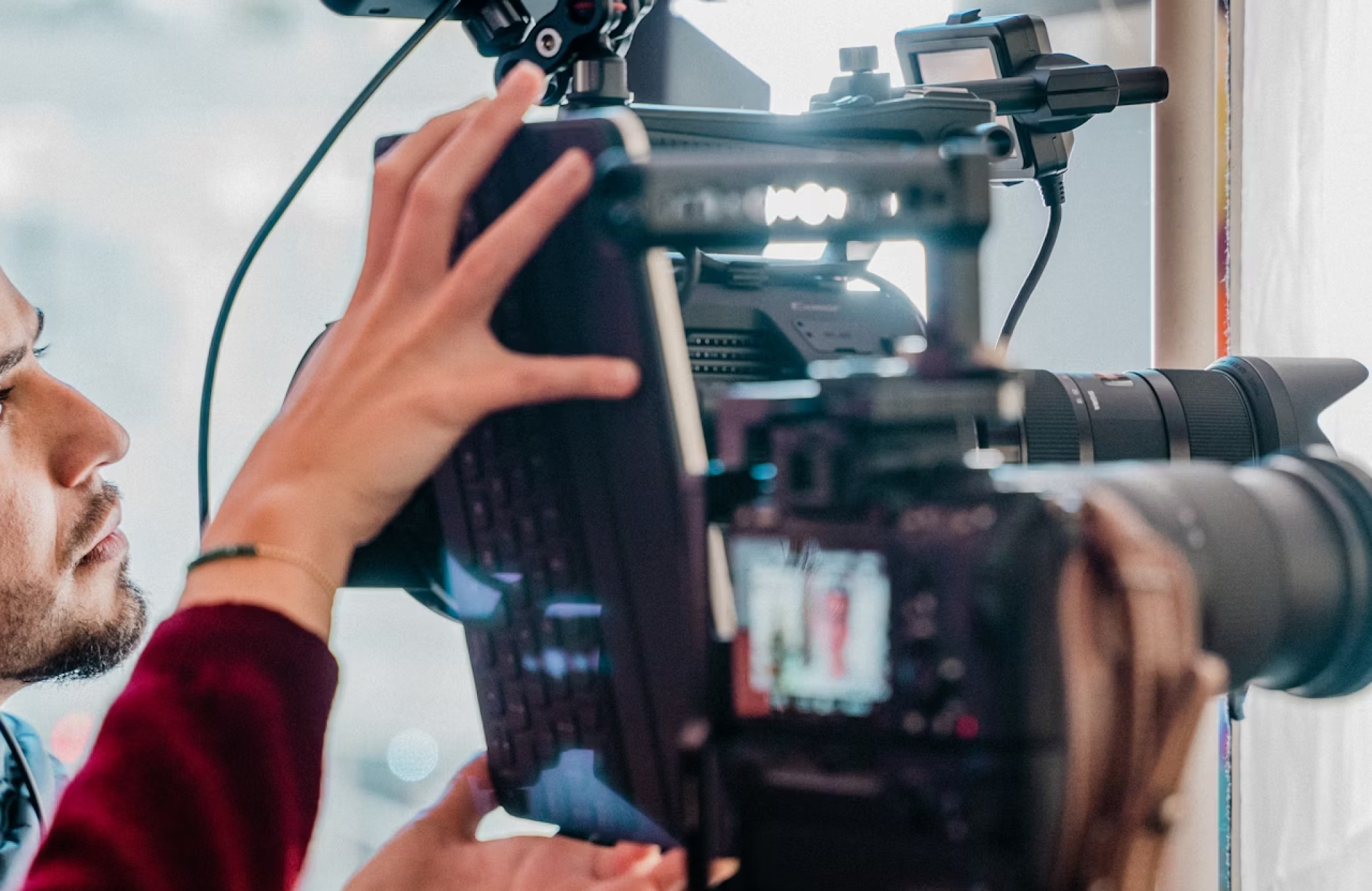 FX Productions Canada A person adjusts a professional video camera setup with attached monitor and lens indoors, highlighting the technical expertise often required by production companies vs agencies. Toronto Video Production Company