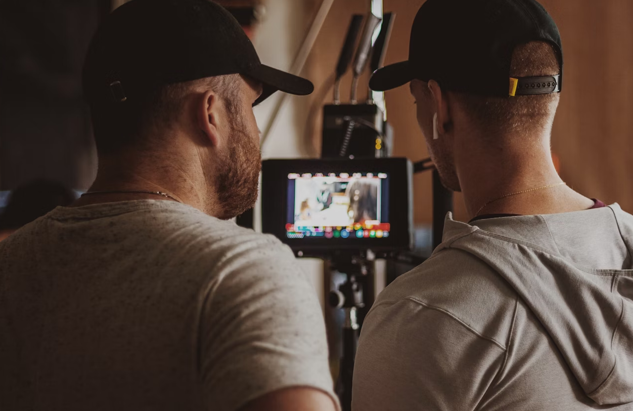 FX Productions Canada Two people in casual clothing and caps stand closely, looking at a video monitor displaying a blurred scene on a film or video production set. Toronto Video Production Company
