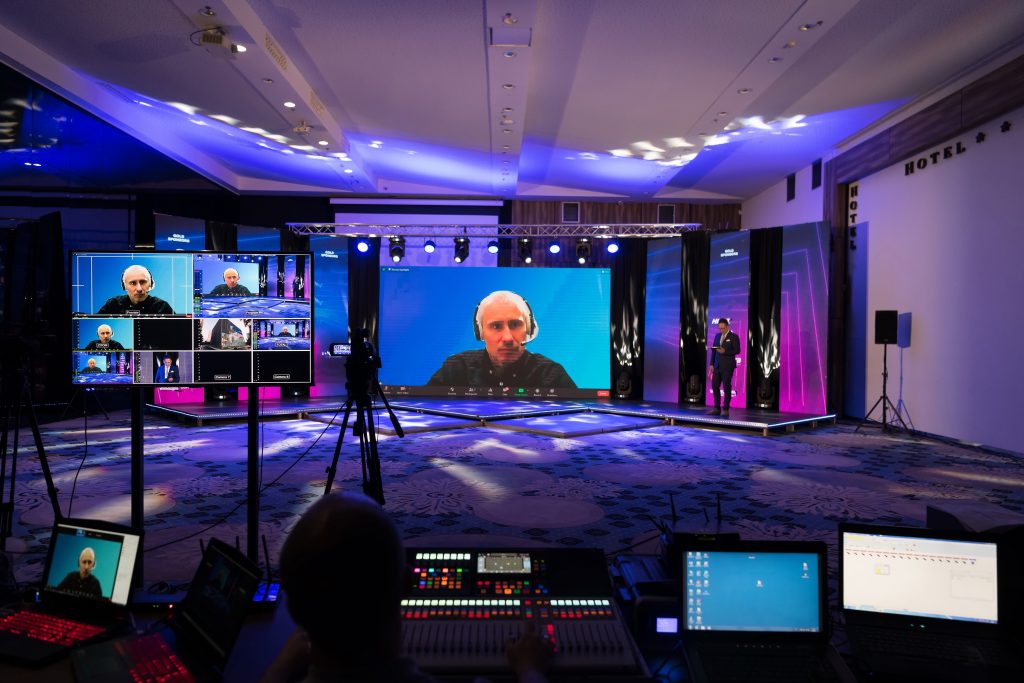 FX Productions Canada A man wearing a headset appears on large screens during a virtual conference, with technical equipment and crew visible in a dimly lit event space. Toronto Video Production Company
