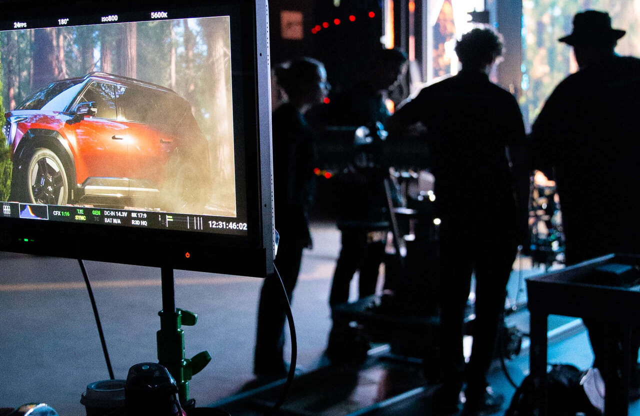 FX Productions Canada A monitor displays a red SUV in a forest scene while a film crew stands and works in silhouette in the background on a production set. Toronto Video Production Company