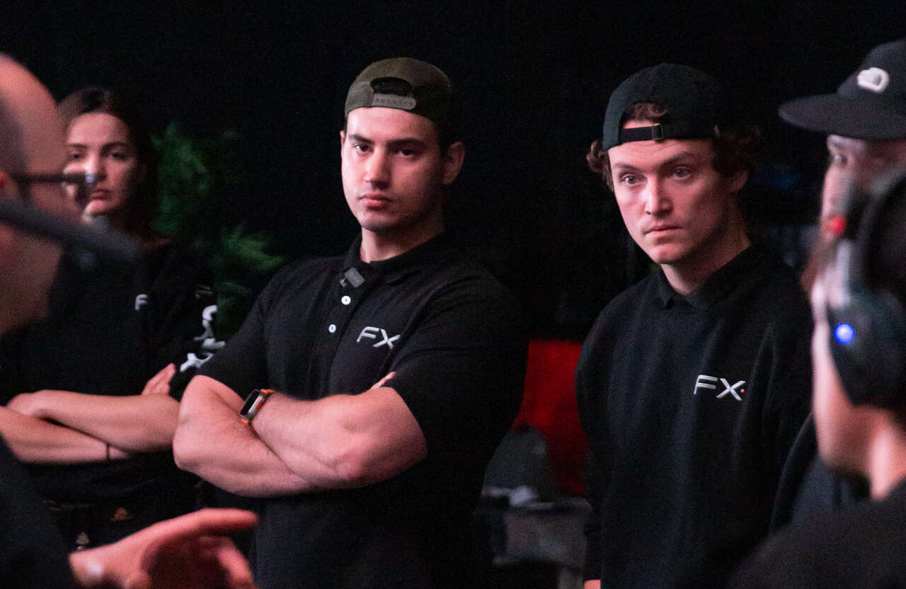 FX Productions Canada A group of people in black FX-branded shirts stand and listen attentively, with two men in the center crossing their arms and facing someone speaking off camera. Toronto Video Production Company
