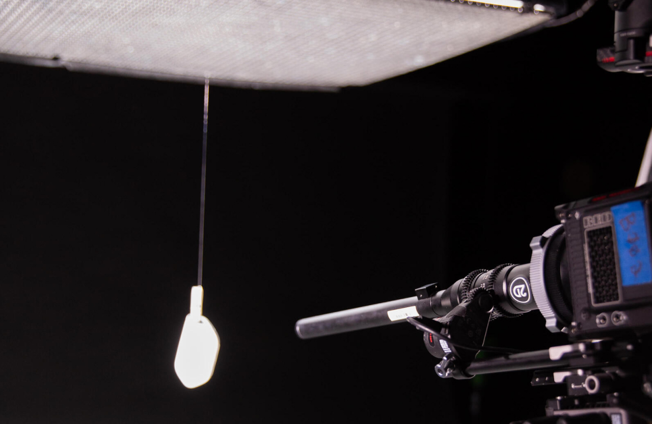 FX Productions Canada A camera on a tripod is aimed at a lit lightbulb hanging from a cord in front of a softbox or diffuser against a dark background. Toronto Video Production Company