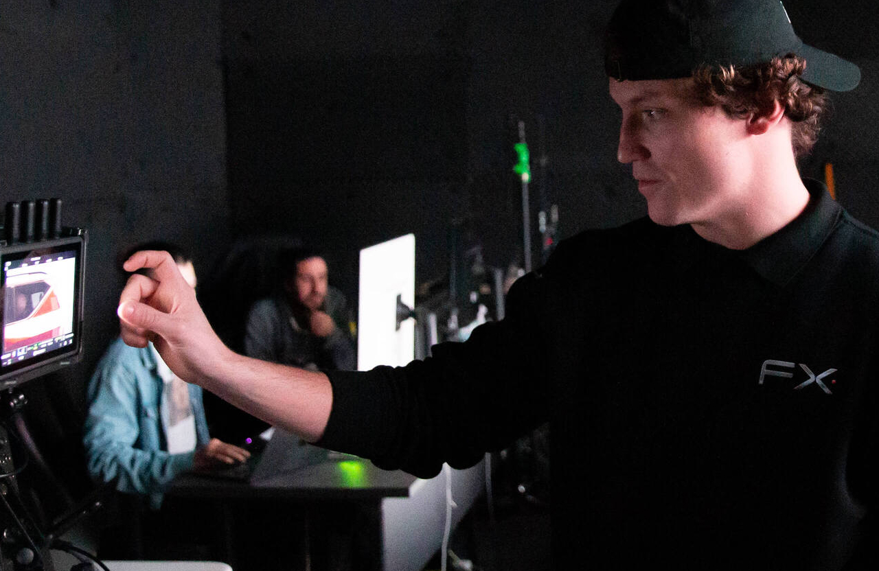FX Productions Canada A person wearing a black FX shirt and cap adjusts a monitor, while two people work at computers in the background in a dimly lit room. Toronto Video Production Company