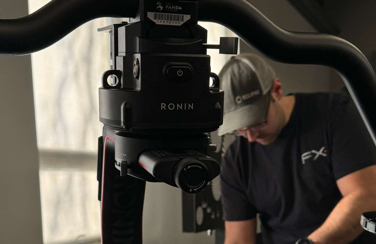 FX Productions Canada A close-up of a Ronin camera stabilizer; a person wearing a cap and glasses is seen working in the blurred background. Toronto Video Production Company