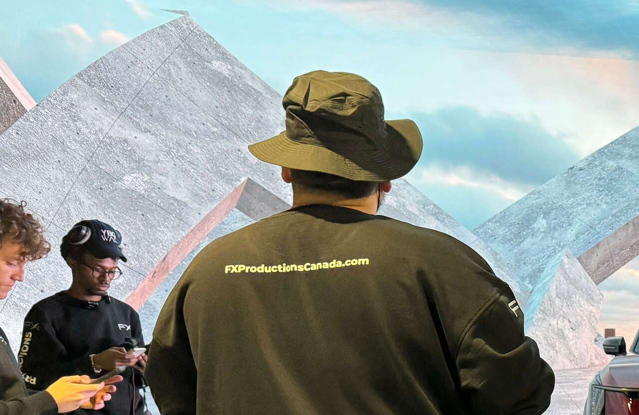 FX Productions Canada Three people stand near abstract concrete structures; the central figure wears a black hat and jacket labeled "FXProductionsCanada.com" on the back. Toronto Video Production Company