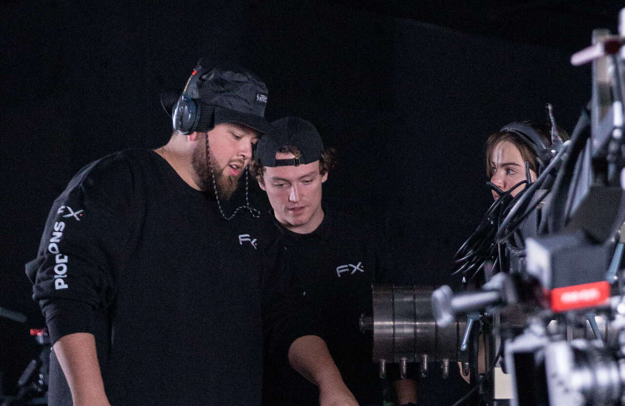 FX Productions Canada Three people in black clothing and headsets operate and discuss equipment on a film or TV production set in a dimly lit environment. Toronto Video Production Company
