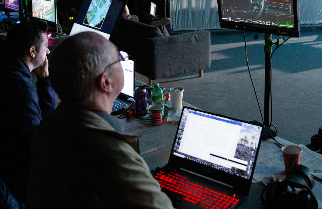 FX Productions Canada Two people sit at a table with laptops and monitors, working in a dimly lit room filled with equipment and drinks. Toronto Video Production Company