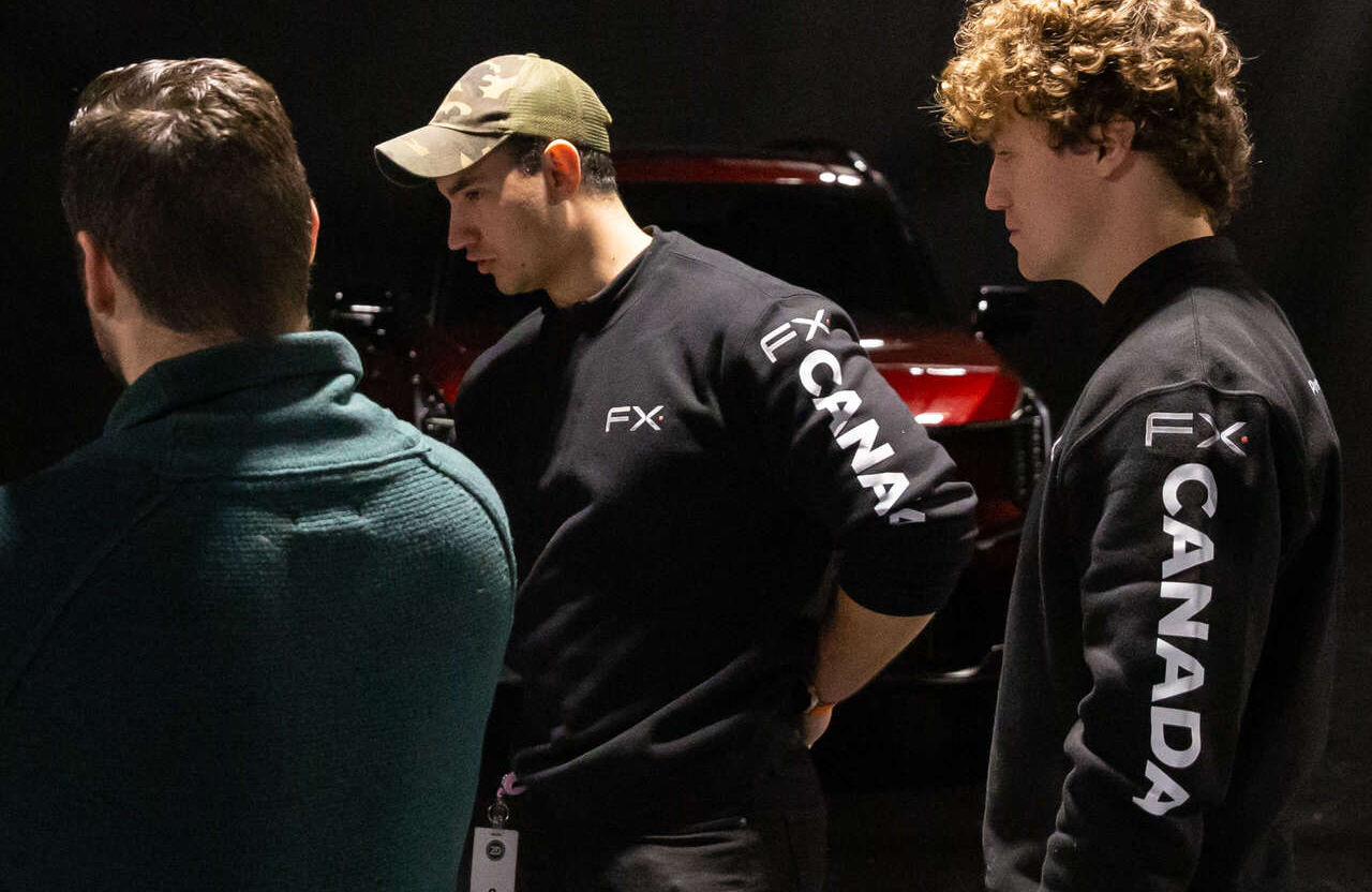 FX Productions Canada Three men stand indoors near a red vehicle. Two wear black FX Canada sweatshirts, and one wears a green cap. The background is dimly lit. Toronto Video Production Company
