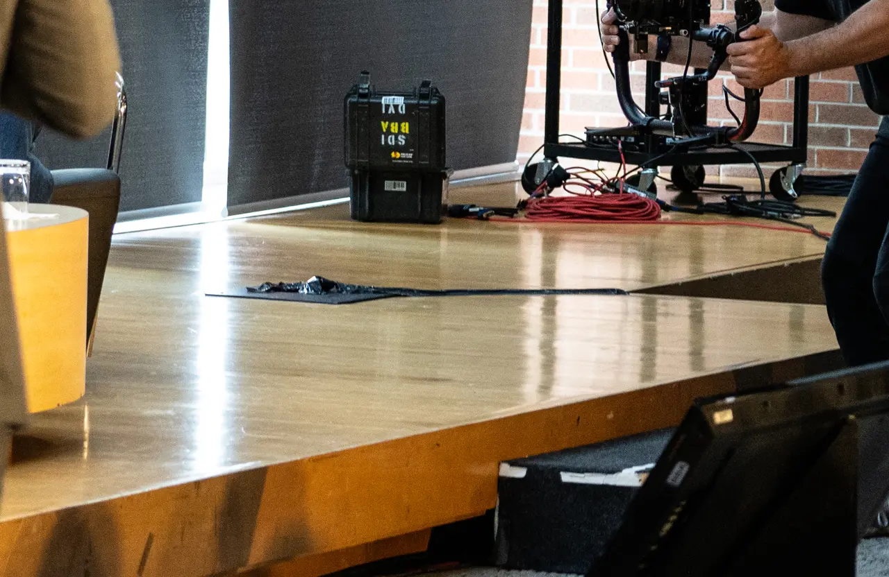 FX Productions Canada A thick black cable runs across a wooden stage floor, with camera equipment and a coiled red cable in the background—capturing the behind-the-scenes of corporate video production in Toronto. Toronto Video Production Company