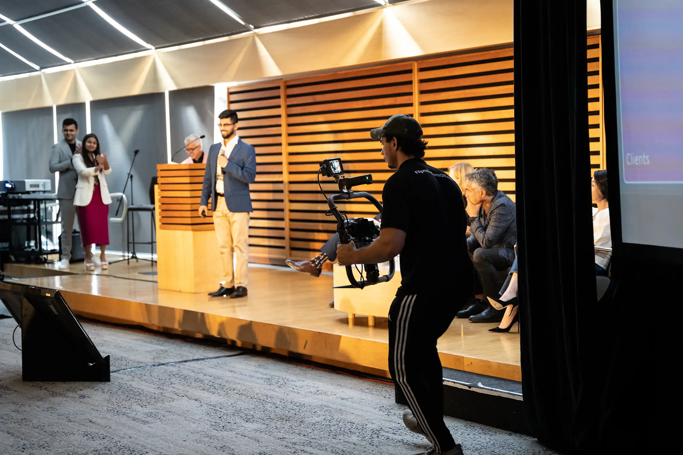 FX Productions Canada A cameraman from a production partner Toronto team films a group of people on stage during a presentation or panel discussion in a modern conference room. Toronto Video Production Company