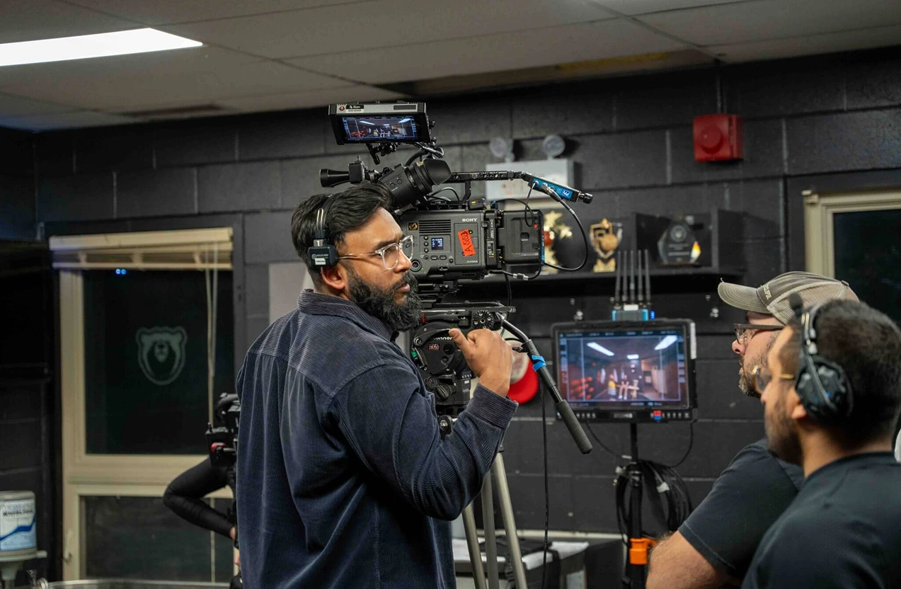 FX Productions Canada A cameraman with headphones operates a professional video camera indoors, while two other crew members stand nearby in a studio setting—perfect for hybrid and remote workforce video production needs. Toronto Video Production Company