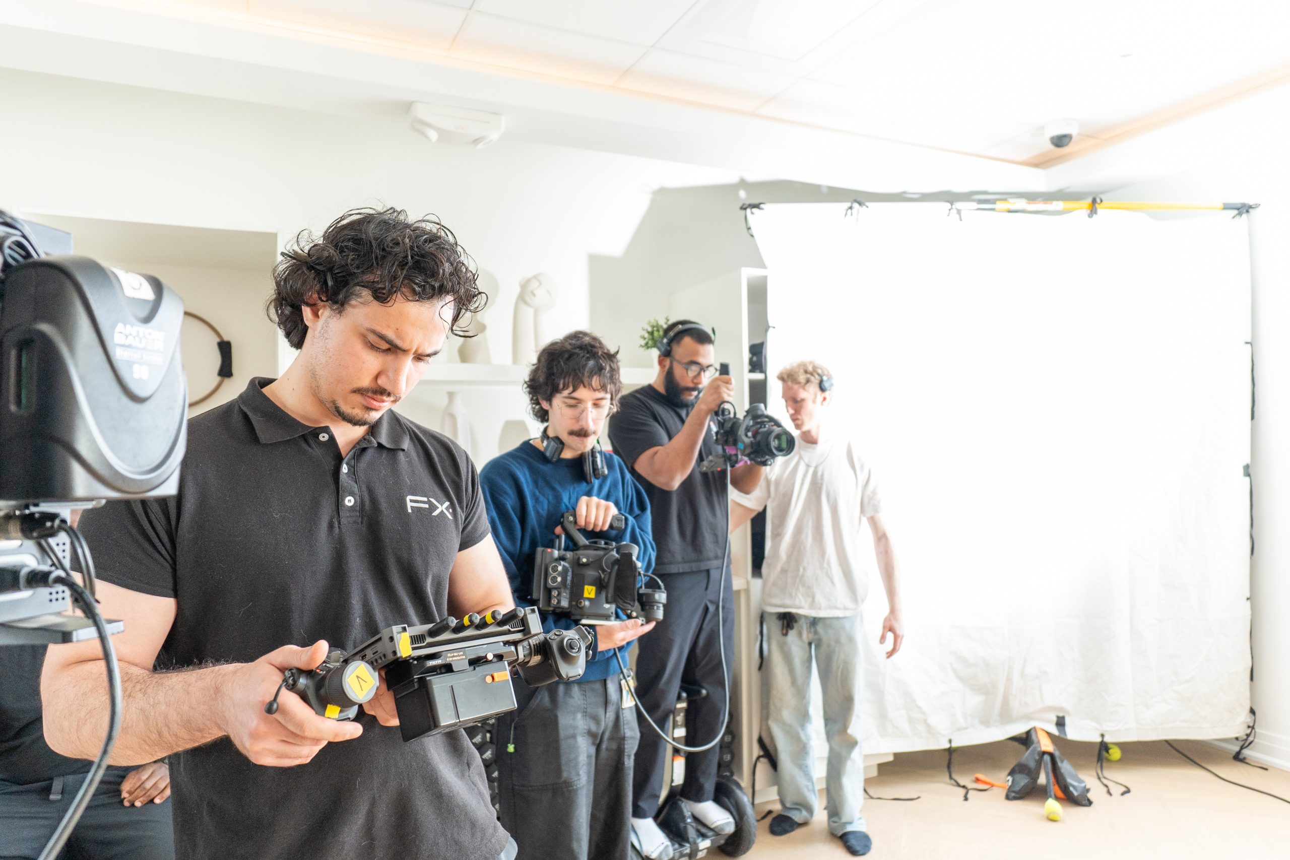 FX Productions Canada Four crew members operate cameras and equipment on a brightly lit film set, with a large white backdrop and various technical gear visible. Toronto Video Production Company
