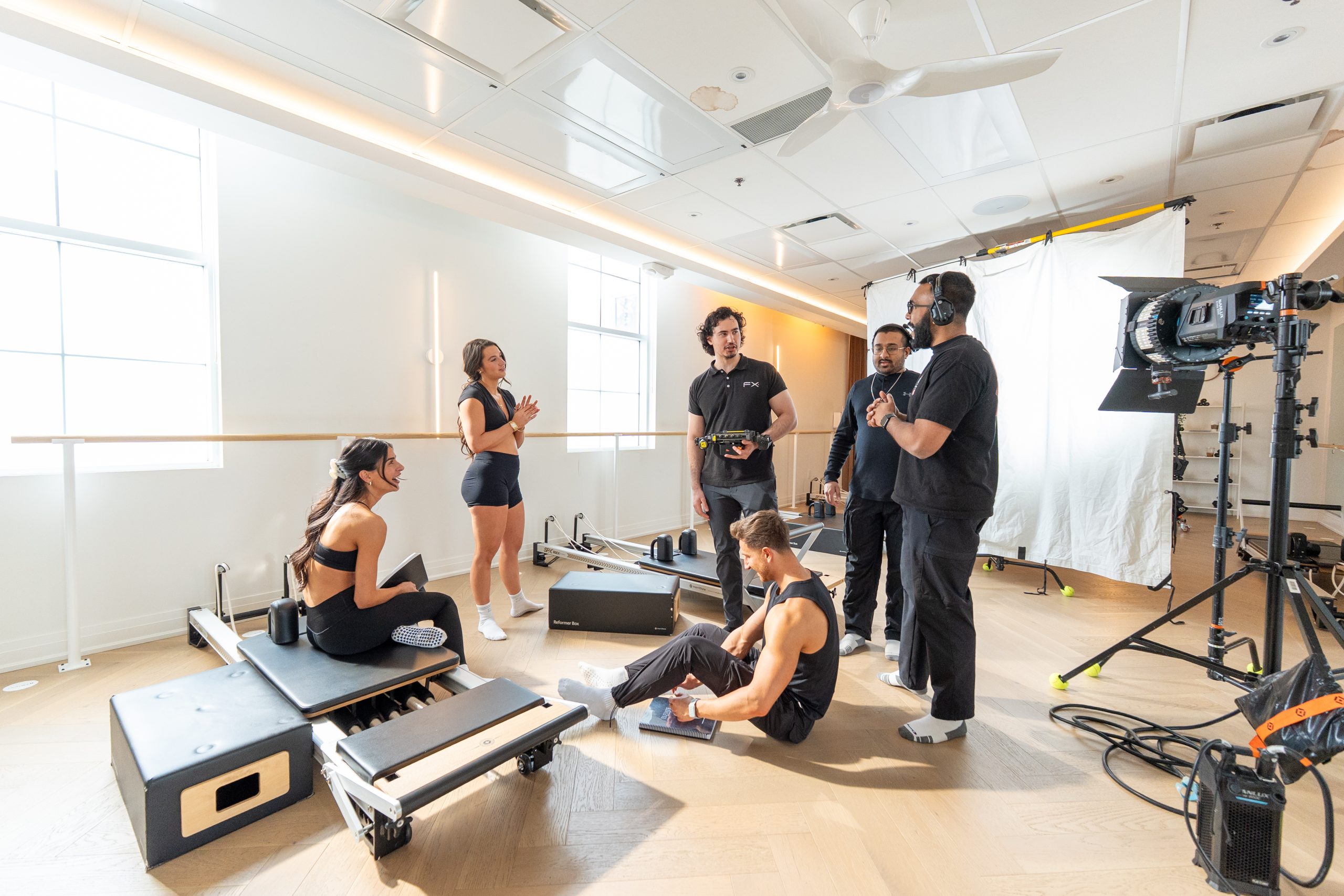 FX Productions Canada A group of people in athletic wear interact with a film crew in a brightly lit fitness studio with equipment and cameras visible. Toronto Video Production Company