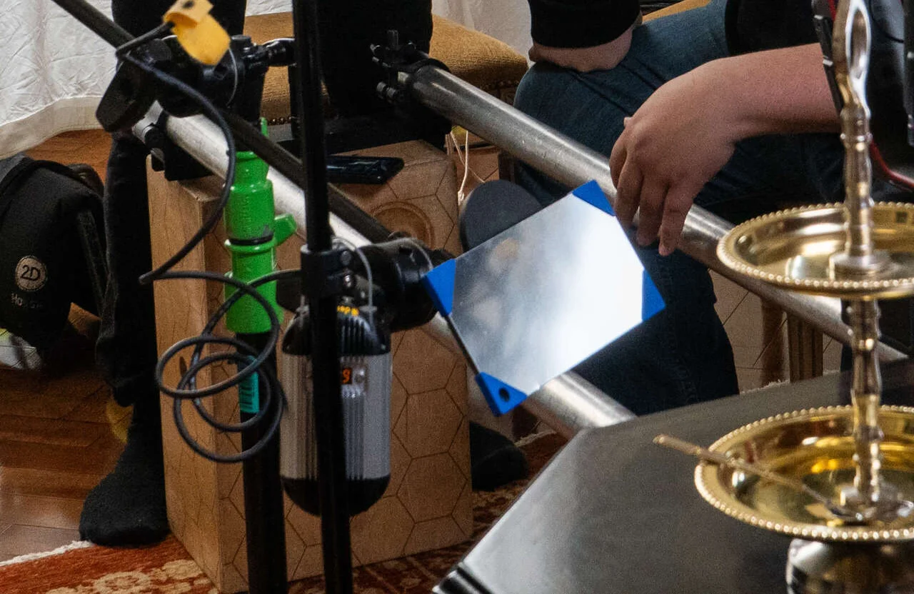 FX Productions Canada A close-up of a film set highlights lighting equipment, a reflector, and part of a gold-colored prop on a table—crew members in the background adjust gear as part of a full service video production workflow. Toronto Video Production Company