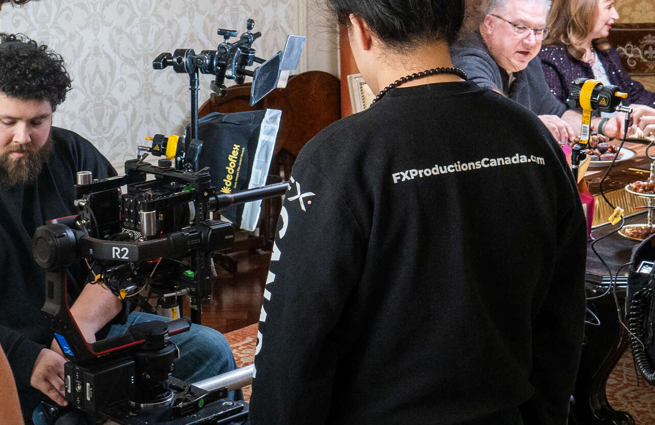 FX Productions Canada Film crew operating cameras and equipment on set, with people seated at a table in the background. A crew member's shirt reads "FXProductionsCanada.com," highlighting their role as a full service video production partner. Toronto Video Production Company