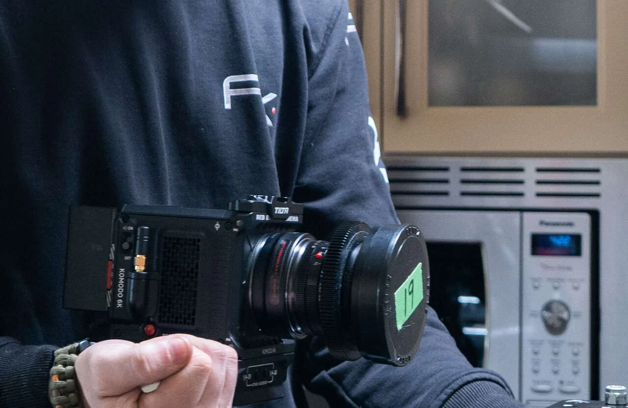 FX Productions Canada A person holds a professional video camera in a kitchen, with a microwave and oven in the background, highlighting the difference between full service vs piecemeal video production approaches. Toronto Video Production Company