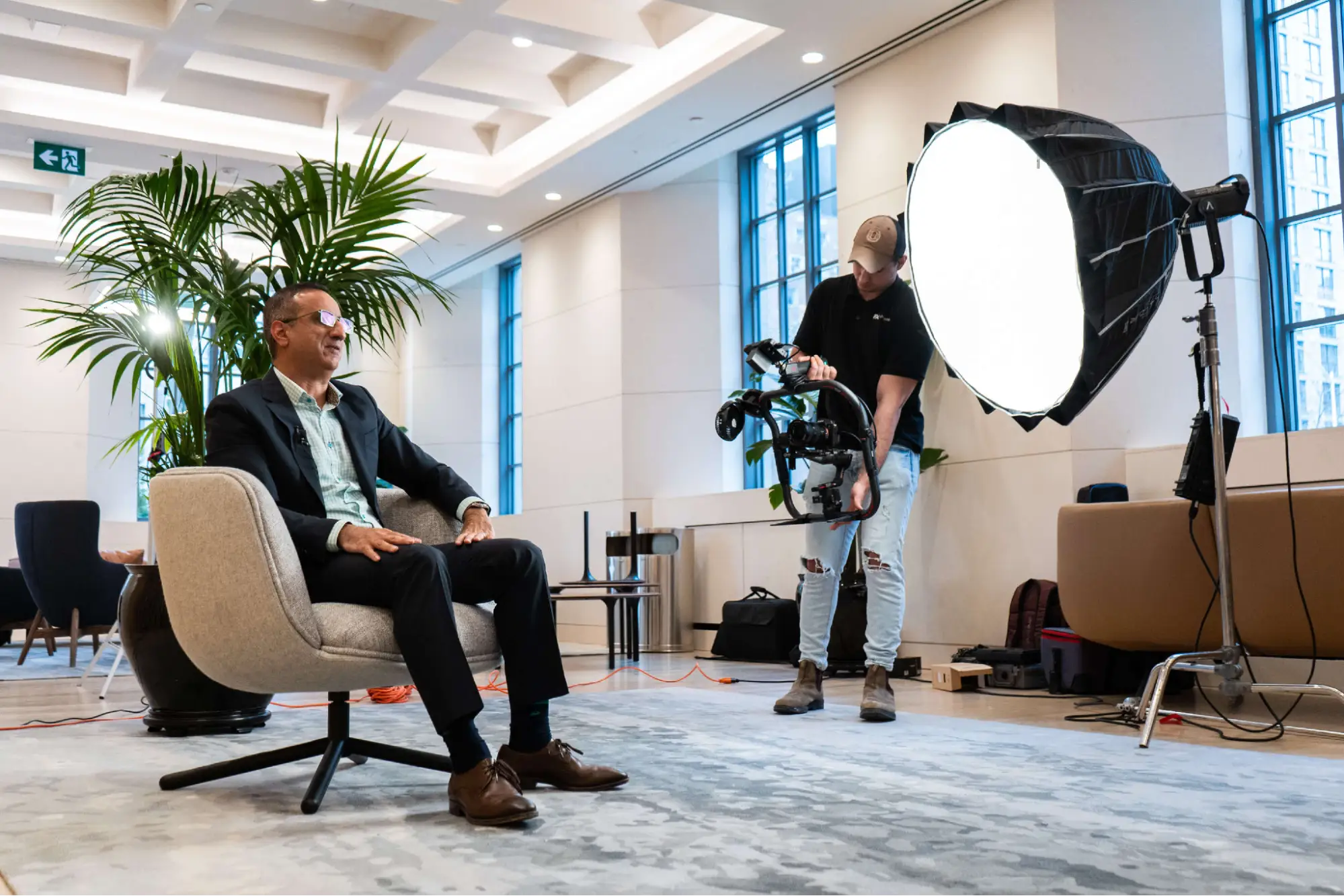 FX Productions Canada A man in a suit sits in a modern office while another person operates a camera and studio light, preparing for a corporate video production in Toronto. Toronto Video Production Company